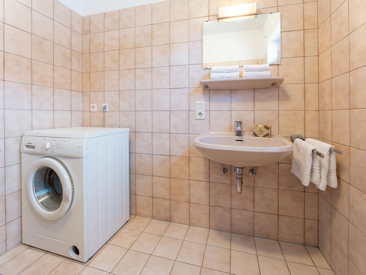 Waschmaschine neben Waschbecken mit Spiegel und Handtüchern in gefliestem Badezimmer
